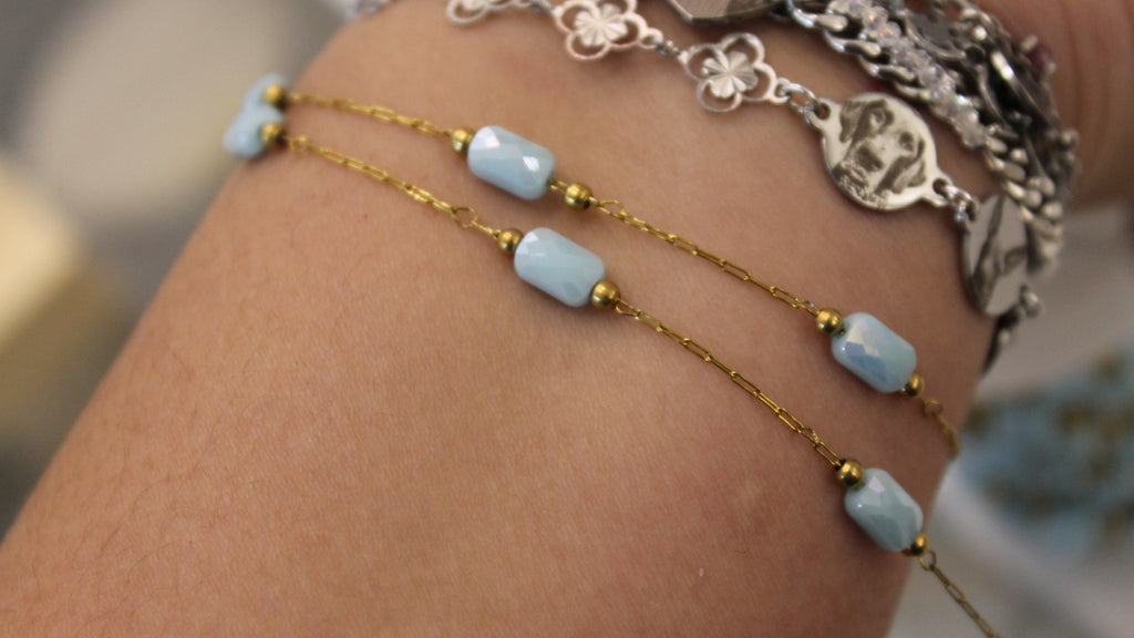 Close-up of a wrist wearing gold chain bracelets with blue gems.