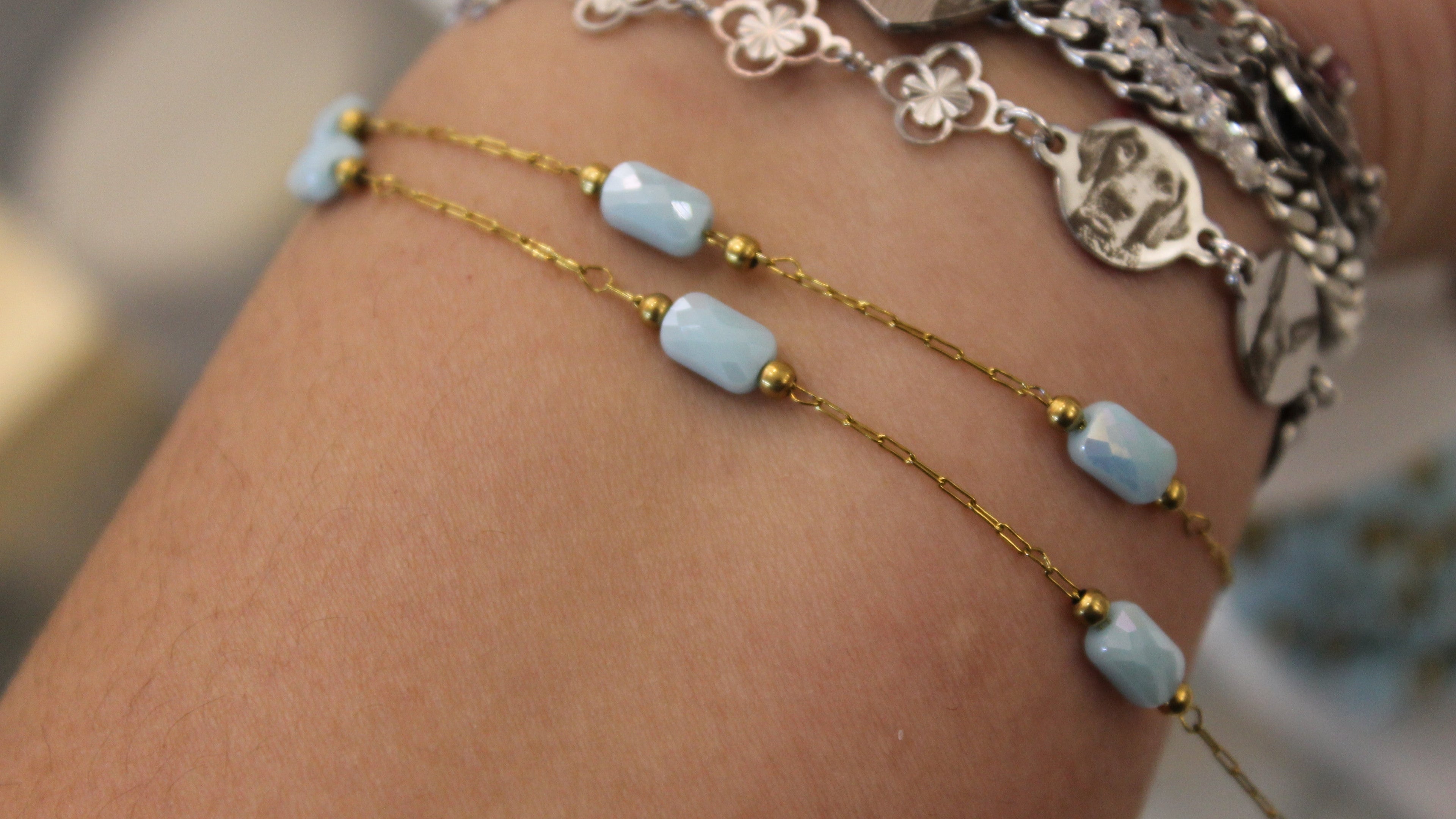 Close-up of a wrist wearing gold chain bracelets with blue gems.